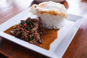 revuelva la carne frita con albahaca con huevo frito en un plato blanco es un simple a la carta. que los tailandeses son muy populares. foto