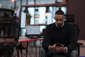 Young African American work in coworking space using smartphone analyzing online market trends, focused man worker reading financial news or browsing internet on phone. Technology concept photo