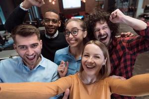 Group of business people during break from the work taking selfie picture while enjoying free time in relaxation area at modern open plan startup office. Selective focus photo