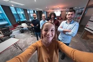 Group of business people during break from the work taking selfie picture while enjoying free time in relaxation area at modern open plan startup office. Selective focus photo