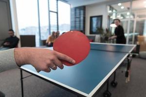 un joven hombre y una mujer de negocios que empiezan a jugar tenis de mesa en un espacio de oficina creativo moderno grupo de personas que se reúnen y hacen una lluvia de ideas en segundo plano foto