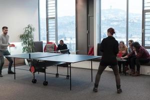 un joven hombre y una mujer de negocios que empiezan a jugar tenis de mesa en un espacio de oficina creativo moderno grupo de personas que se reúnen y hacen una lluvia de ideas en segundo plano foto