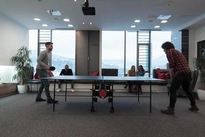 Two young start up business man playing table tennis at modern creative office space people group have meeting and brainstorming in background photo