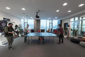 Man with camera recording two young business man playing ping pong tennis at modern creative office space people group have meeting and brainstorming in background photo