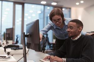 Young smiling woman explaining to serious African American coworker project strategy. Diverse startup coworkers students woman and man talking discussing working in modern office using computer. photo