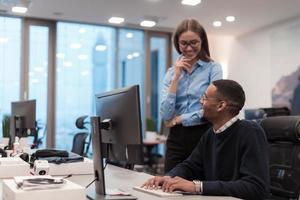 Young smiling woman explaining to serious African American coworker project strategy. Diverse startup coworkers students woman and man talking discussing working in modern office using computer. photo