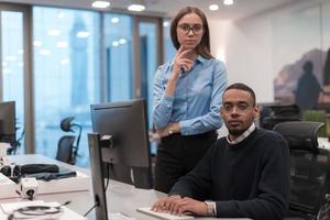 Young smiling woman explaining to serious African American coworker project strategy. Diverse startup coworkers students woman and man talking discussing working in modern office using computer. photo