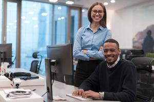 joven mujer sonriente explicando a una seria estrategia de proyecto de compañeros afroamericanos. diversos compañeros de trabajo de inicio estudiantes mujer y hombre hablando discutiendo el trabajo en la oficina moderna usando la computadora. foto