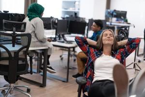 Casual business woman taking a break with legs on her table while working on desktop computer in modern open plan startup office interior. Selective focus photo