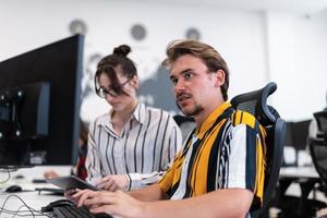 Business couple working together on project using tablet and desktop computer at modern open plan startup office. Selective focus photo