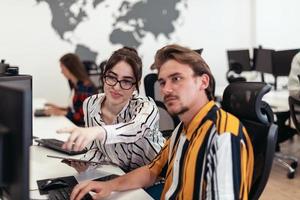 Business couple working together on project using tablet and desktop computer at modern open plan startup office. Selective focus photo