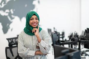 Portrait of muslim black female software developer with green hijab standing at modern open plan startup office. Selective focus photo