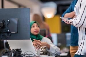 Multiethnic startup business team Arabian woman wearing a hijab on meeting in modern open plan office interior brainstorming, working on laptop and desktop computer. Selective focus photo