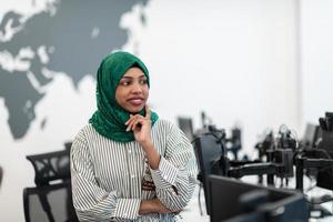 Portrait of muslim black female software developer with green hijab standing at modern open plan startup office. Selective focus photo