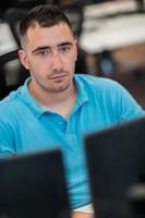Casual business man working on desktop computer in modern open plan startup office interior. Selective focus photo