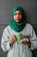 African Muslim businesswoman with green hijab using mobile phone during coffee break from work outside photo