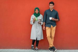 grupo multiétnico de gente de negocios casual que usa un teléfono inteligente durante el descanso para tomar café del trabajo frente a la pared roja afuera foto