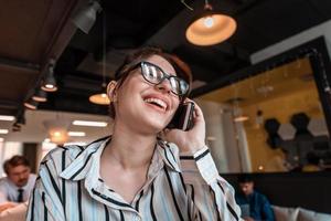 Businesswoman with glasses using mobile phone at modern startup open plan office interior. Selective focus photo