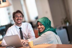 equipo de negocios multicultural internacional. hombre y mujer musulmana con hiyab trabajando juntos usando el área de coxación de teléfonos inteligentes y computadoras portátiles en la oficina de inicio de plan abierto moderno en rela foto