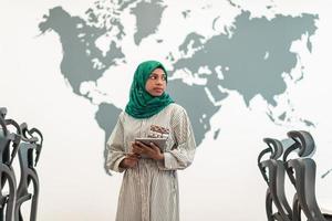 Portrait of muslim female software developer with green hijab holding tablet computer while standing at modern open plan startup office photo