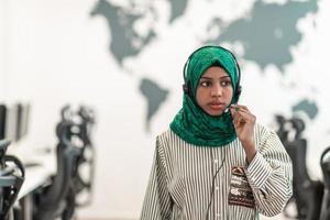 mujer afro musulmana con bufanda hijab verde representante del cliente mujer de negocios con auriculares de teléfono ayudando y apoyando en línea con el cliente en un centro de llamadas moderno foto