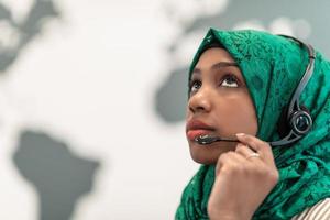 mujer afro musulmana con bufanda hijab verde representante del cliente mujer de negocios con auriculares de teléfono ayudando y apoyando en línea con el cliente en un centro de llamadas moderno foto