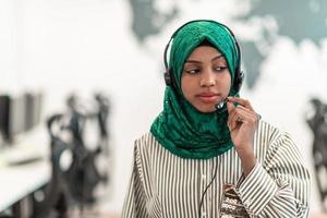 mujer afro musulmana con bufanda hijab verde representante del cliente mujer de negocios con auriculares de teléfono ayudando y apoyando en línea con el cliente en un centro de llamadas moderno foto