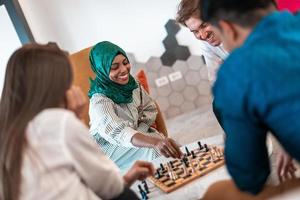 Multiethnic group of business people playing chess while having a break in relaxation area at modern startup office. Selective focus photo