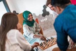 Multiethnic group of business people playing chess while having a break in relaxation area at modern startup office. Selective focus photo