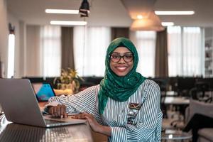 Business woman wearing a green hijab using laptop in relaxation area at modern open plan startup office. Selective focus photo