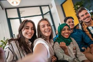 Group of business people during break from the work taking selfie picture while enjoying free time in relaxation area at modern open plan startup office. Selective focus photo