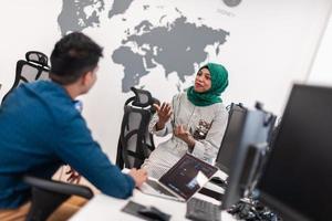 Multiethnic startup business team Arabian woman wearing a hijab on meeting in modern open plan office interior brainstorming, working on laptop and desktop computer. Selective focus photo