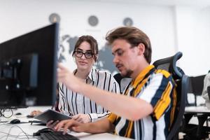 Business couple working together on project using tablet and desktop computer at modern open plan startup office. Selective focus photo