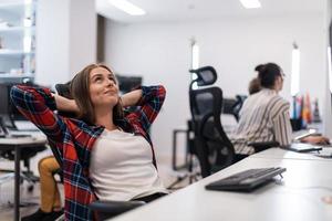 Casual business woman taking a break while working on desktop computer in modern open plan startup office interior. Selective focus photo