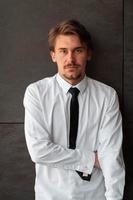 retrato de un nuevo hombre de negocios con una camisa blanca y una corbata negra parado frente a una pared gris afuera