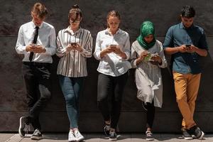 Multiethnic group of casual business people using mobile phone during coffee break from work in front of black wall outside photo