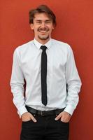 retrato de un nuevo hombre de negocios con una camisa blanca y una corbata negra parado frente a una pared roja afuera foto