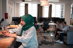 African Muslim business woman wearing a green hijab and working on laptop computer in relaxation area at modern open plan startup office. photo