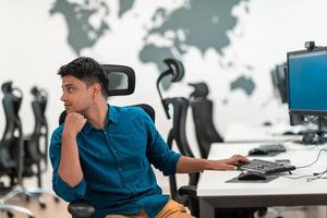 Casual business man working on desktop computer in modern open plan startup office interior. Selective focus photo