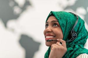 Afro Muslim female with green hijab scarf customer representative business woman with phone headset helping and supporting online with customer in modern call centre photo