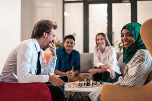 Multiethnic group of business people playing chess while having a break in relaxation area at modern startup office. photo