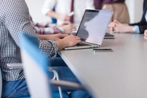 primer plano de las manos del hombre de negocios escribiendo en la computadora portátil con el equipo en la reunión en segundo plano foto