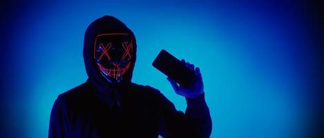 Anonymous hacker and face mask with smartphone in hand. photo