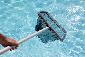 Male hand cleaning a swimming pool with a Skimmer net photo