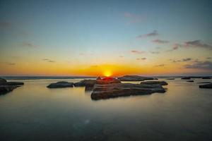 fotografía de larga exposición de olas y guijarros en la playa al atardecer foto