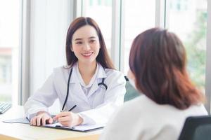 Asian professional doctor woman who wears medical coat talks with female patient to suggest treatment guideline and healthcare concept in office of hospital. photo