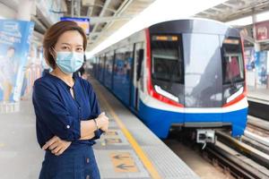 Asian woman who has short hair and wears blue shirt stands arm cross while waiting train at station and wears medical face mask to protect COVID-19 in health care,pollution PM2.5,new normal concept.