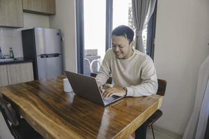 A young Asian man spends his time at home sitting in the dining room working on his laptop feel frustrated photo