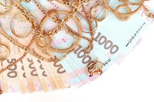 muchos costosos anillos, aretes y collares de joyería de oro con una gran cantidad de billetes de dinero ucraniano. concepto de tienda de empeño o joyería. comercio de joyas foto