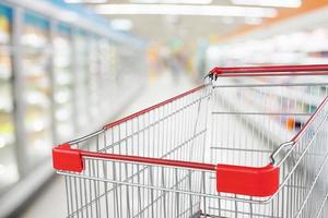 Supermarket aisle blur defocused background with empty red shopping cart photo